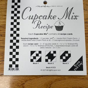 May include: A white square Moda Fabrics Cupcake Mix Recipe 3 card featuring black text and graphics. It lists 44 recipe cards, required ingredients including 5-inch charm packs, and instructions for creating three distinct quilt block patterns.