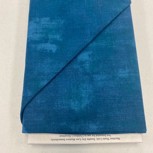 May include: A folded piece of blue fabric with a textured, brushed look. The fabric has a care label that reads "Machine Wash Cold. Tumble Dry Low. Remove Immediately. Not Intended for use in Children's Sleepwear."