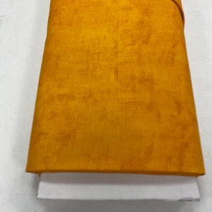 May include: A folded piece of fabric in a solid mustard yellow color. The fabric has a subtle texture and a slightly sheen finish.