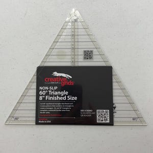 May include: A clear, triangular Creative Grids ruler with measurements and a black label. The label reads "NON-SLIP 60° Triangle 8" Finished Size." The ruler is designed for quilting and crafting.