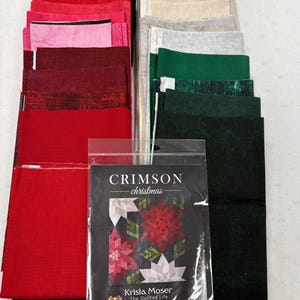 May include: A selection of fabric squares in shades of red, pink, and green, with a pattern packet labelled "Crimson Christmas" by Krista Moser. The packet shows a quilt design with red poinsettias and white geometric shapes.