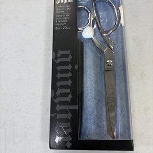 May include: A pair of Gingher knife-edge dressmaker shears in a clear plastic package. The shears are 8 inches long and have a silver finish. The packaging includes the Gingher logo and product information.