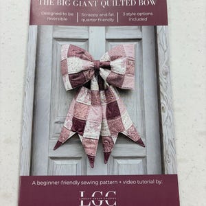 May include: A sewing pattern titled "THE BIG GIANT QUILTED BOW" featuring a large, quilted bow in shades of pink and burgundy. The pattern includes instructions for reversible designs and is beginner-friendly. The text on the pattern reads "Designed to be reversible" and "Scrappy and fat quarter friendly."