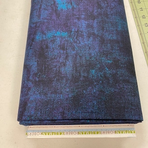 May include: A close-up of a dark blue fabric with a subtle textured pattern. The fabric has a slight sheen and is folded in half. The fabric is labeled "Robert Kaufman" and has a website address printed on the label.