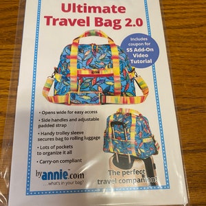 May include: A colorful travel bag with a floral pattern and a trolley sleeve. The bag has side handles, lots of pockets, and is carry-on compliant. The text "Ultimate Travel Bag 2.0" and "byannie.com" is printed on the front of the bag. The text "The perfect travel companion!" is printed below the bag.