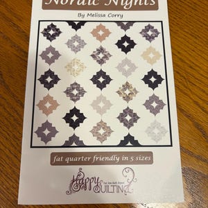 May include: A quilting pattern titled "Nordic Nights" by Melissa Corry. The pattern features a quilt design with a geometric pattern in shades of gray, brown, and white. The pattern is fat quarter friendly and available in five sizes. The pattern is from Happy Quilting.