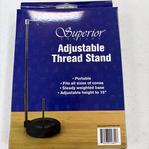 May include: A black adjustable thread stand with a weighted base, designed to hold thread cones. The packaging features the text "Superior Threads Adjustable Thread Stand" and highlights features like portability and adjustable height up to 38 cm.