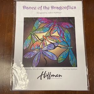 May include: A craft pattern for a quilt featuring a design of four colorful dragonflies with stained glass-like wings. The pattern is titled "Dance of the Dragonflies" and is designed by JoAnn Hoffman. The finished size of the quilt is 40 inches by 40 inches.