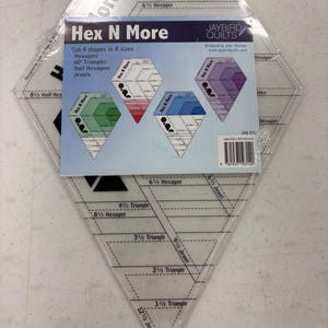 May include: A clear acrylic quilting template with the text "Hex N More" and diagrams for cutting shapes. The template includes measurements for hexagons, triangles, and jewels. The package also includes a card with diagrams.