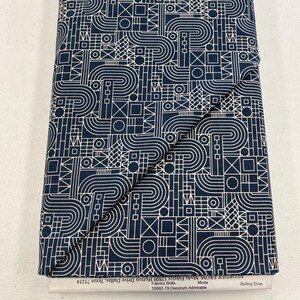 May include: A navy blue fabric with a white geometric pattern. The pattern includes circles, squares, triangles, and lines. The fabric is folded in half and the text "Quilting Divas" is visible on the bottom right corner.