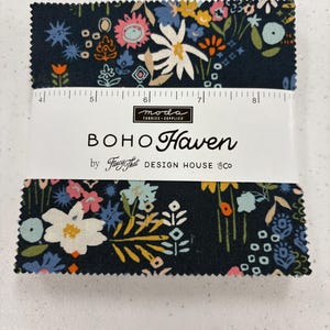 May include: A bundle of fabric squares with a floral pattern in navy, white, pink, orange, and blue. The fabric is wrapped with a white label that reads "BOHO Haven" and "by Fancy That DESIGN HOUSE & CO."