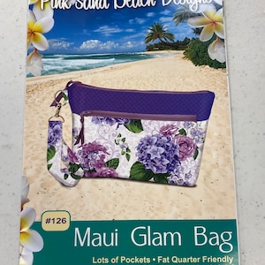 May include: A sewing pattern for a purple and white floral bag with the title "Maui Glam Bag" and the text "Lots of Pockets - Fat Quarter Friendly - Color Picture Instructions Included". The pattern is designed by Nancy Green - Pink Sand Beach Designs.
