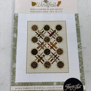 May include: A quilt pattern titled "Windfall" featuring a sunflower plaid design. The finished size is 58" x 76 1/2". The pattern includes a design with brown, beige, and cream colors. The Moda Fabrics Windfall Collection is featured.