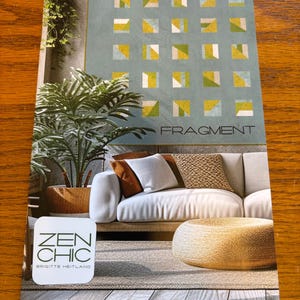 May include: A white sofa with brown pillows sits in a room with a green plant and a gold ottoman. The wall behind the sofa has a geometric pattern of squares in shades of blue, green, and yellow. The text "FRAGMENT" is printed in black on the wall. The text "ZEN CHIC" is printed in green on a white square below the sofa. The text "BRIGITTE HEITLAND" is printed in black below the "ZEN CHIC" text.