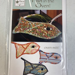 May include: A sewing pattern for a set of three oven mitts shaped like fish. The mitts are made of colorful fabric with a variety of patterns. The pattern is called "Fish in the Oven!" and is from Vanilla House Designs.