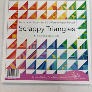 May include: A package of "Scrappy Triangles" foundation papers for paper piecing. The cover features a grid of colorful triangles in various patterns. The text reads "Foundation Papers for 50 Different Paper-Pieced" and "6" Finished Block Size".