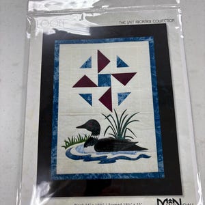 May include: A sewing pattern for a quilt featuring a loon in a lake, with a geometric design above. The quilt block measures 14" x 19.5", framed at 19.5" x 25". The text "THE LAST FRONTIER COLLECTION" and "MANOAH Sewing Pattern" are visible.