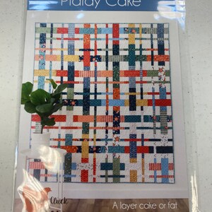 May include: A quilting pattern called "Plaidy Cake" by Cluck Sew. The pattern is for a layer cake or fat quarter quilt in 5 sizes. The quilt design features a colorful plaid pattern with red, orange, yellow, blue, green, and black squares.