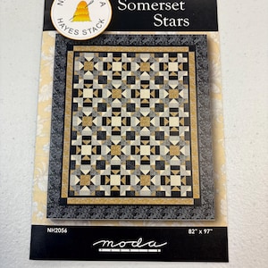 May include: A quilt pattern titled "Somerset Stars" by Needle in a Hayes Stack. The design features a repeating pattern of black, gold, and cream-colored squares and triangles. The quilt measures 82" x 97". The Moda Fabrics logo is at the bottom.