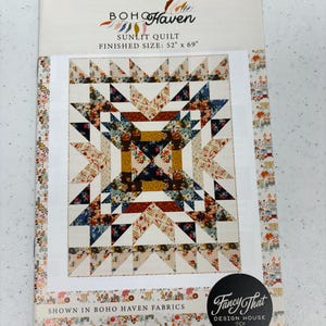 May include: A quilt pattern titled "Sunlit Quilt" by Boho Haven, with a finished size of 132 cm x 175 cm. The quilt design features a central starburst pattern in shades of cream, navy, and rust. The pattern is shown in Boho Haven fabrics.