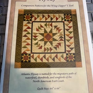 May include: A quilt pattern named "Atlantic Flyway" featuring a star design in beige, green, and red. The quilt size is 112 cm x 112 cm. The pattern is designed for the Wing Clipper I Tool.