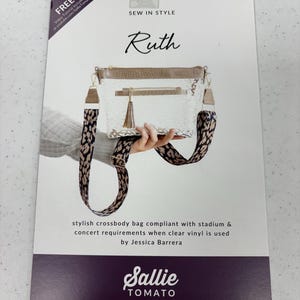 May include: A sewing pattern titled "Ruth" for a stylish crossbody bag. The bag features a clear vinyl body, a brown top, and a patterned strap. The pattern is from Sallie Tomato, with a YouTube tutorial link.