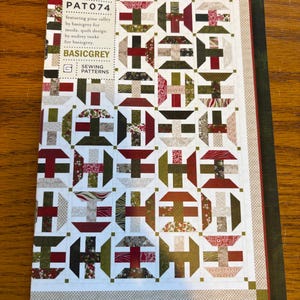 May include: A sewing pattern titled "Lost in the Pines" by BasicGrey. The cover features a quilt design with geometric shapes in shades of red, green, brown, and white. The pattern is PAT074 and includes the text "Sewing Patterns".