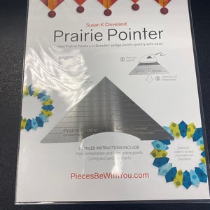 May include: A silver quilting tool called the Prairie Pointer, designed to create prairie points and Dresden wedge points. The tool is packaged in a clear plastic bag with a white background. The text on the packaging reads "Susan K Cleveland Prairie Pointer Create Prairie Points and Dresden wedge points quickly with ease."  The text "PiecesBeWithYou.com" is also on the packaging.