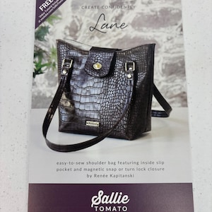 May include: A brochure featuring a brown, textured shoulder bag with a flap closure. The text "Lane" is displayed above the bag, with additional text describing the bag's features and the brand "Sallie Tomato."