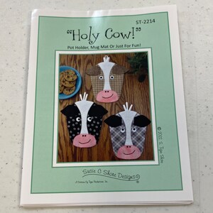May include: A sewing pattern for a "Holy Cow!" pot holder, mug mat, or just for fun. The pattern features three cow faces with different colored and patterned fabrics. The pattern is printed on white paper with a green border.