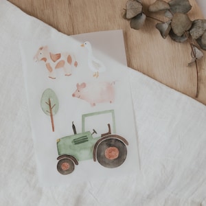 Könnte beinhalten: Ein Set mit Bauernhoftier-Stickern mit einem grünen Traktor, einem rosa Schwein, einer braunen und weißen Kuh und einer weißen Ente. Die Sticker sind auf weißem Hintergrund.