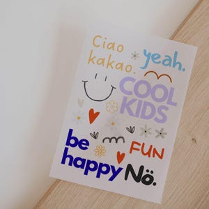 Könnte beinhalten: Ein weißes Papier mit farbenfrohem Text und Illustrationen. Der Text enthält "Ciao kakao," "yeah," "COOL KIDS," "be happy," und "FUN." Es gibt auch Herz- und Blumenillustrationen.