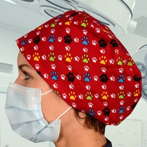 以下が含まれることがあります： 黒、青、緑、黄色の足跡模様の赤い手術帽。帽子は、青いスクラブトップと薄い青色の外科用マスクを着用した人がかぶっています。