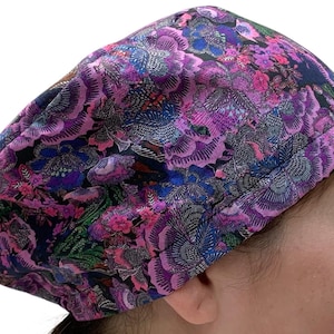 May include: A patterned cap with a floral design in purple, pink, blue, and green. The cap has a repeating pattern of stylized flowers and leaves on a black background. The cap is made of a soft, flexible fabric.