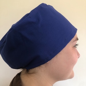 May include: A navy blue surgical scrub cap. The cap is made of a smooth fabric and is designed to cover the hair during medical procedures. The cap is worn on the head.