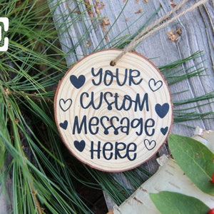 Może przedstawiać: Okrągła drewniana ozdoba z napisem "Your Custom Message Here" i kilkoma czarnymi sercami namalowanymi na niej. Ozdoba jest zawieszona na sznurku jutowym.