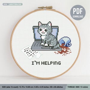 Könnte beinhalten: Kreuzstich-Stickerei in einem Holzrahmen. Das Design zeigt eine graue Katze, die auf einem Laptop sitzt, mit dem Text "I'M HELPING" darunter. Rechts ist eine verschüttete Kaffeetasse dargestellt. Das Design misst 12,70 x 10,80 cm.