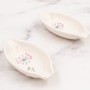 May include: Two white ceramic dishes with a floral design. The dishes are shaped like a boat and have a pink and gray floral design.