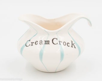 May include: White ceramic creamer with a blue and white striped design. The creamer has a handle and says "Cream Crock" on the front.