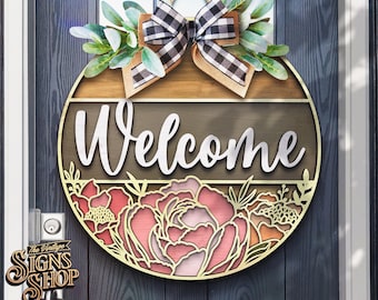 May include: A round wooden welcome sign with a black and white checkered bow and floral accents. The sign says "Welcome" in white lettering.