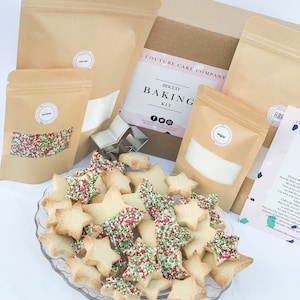 May include: A biscuit baking kit containing all the ingredients and supplies needed to make Christmas-themed cookies. The kit includes flour, sugar, sprinkles, and cookie cutters. The kit is packaged in a brown box with the words "Couture Cake Company" printed on the side.