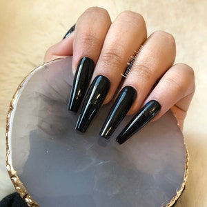 May include: Long, black, glossy, coffin-shaped press-on nails on a white marble-like nail art display with a gold rim.