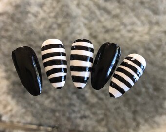 May include: Five black and white striped oval-shaped false nails. Two of the nails are solid black.