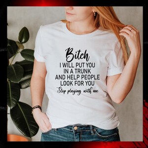 May include: White t-shirt with the text "Bitch I will put you in a trunk and help people look for you. Stop playing with me" in black script. The shirt is worn by a person.