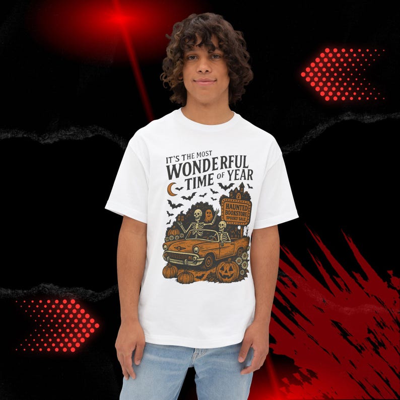 May include: White t-shirt with a Halloween-themed graphic. The design features a vintage orange car with skeletons, pumpkins, bats, and the text "IT'S THE MOST WONDERFUL TIME OF YEAR." A sign reads "Haunted Bookstore Spooky Sale."