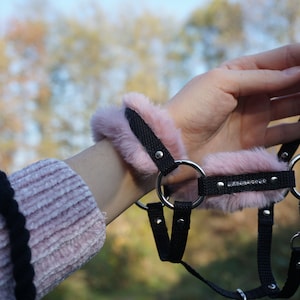 May include: A black faux fur choker with pink fur trim and silver hardware. The choker has a small silver clasp and a decorative rhinestone strip.