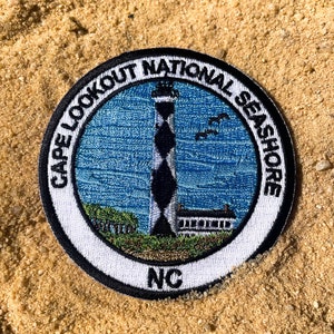 May include: A black and white embroidered patch with a lighthouse, the words "Cape Lookout National Seashore" and "NC".