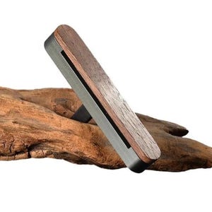 May include: A wooden and metal phone stand with a dark wood finish. The stand is designed to hold a phone in a vertical position.
