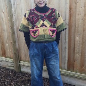 Puede incluir: Una persona lleva una camisa de patchwork multicolor con detalles en rosa, un jersey de cuello alto negro, vaqueros azules y botas marrones. La camisa tiene un patrón geométrico con colores rojo, verde y amarillo.