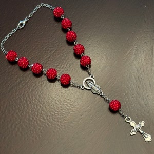 May include: A red crystal rosary with a silver charm and a silver cross.